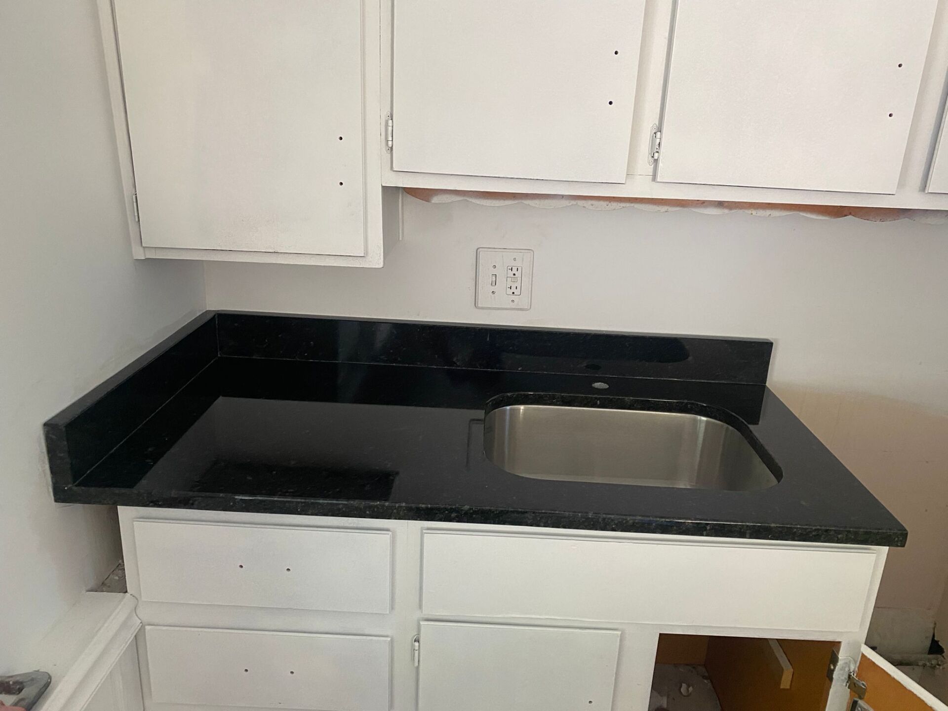 A kitchen with a black counter top and a stainless steel sink