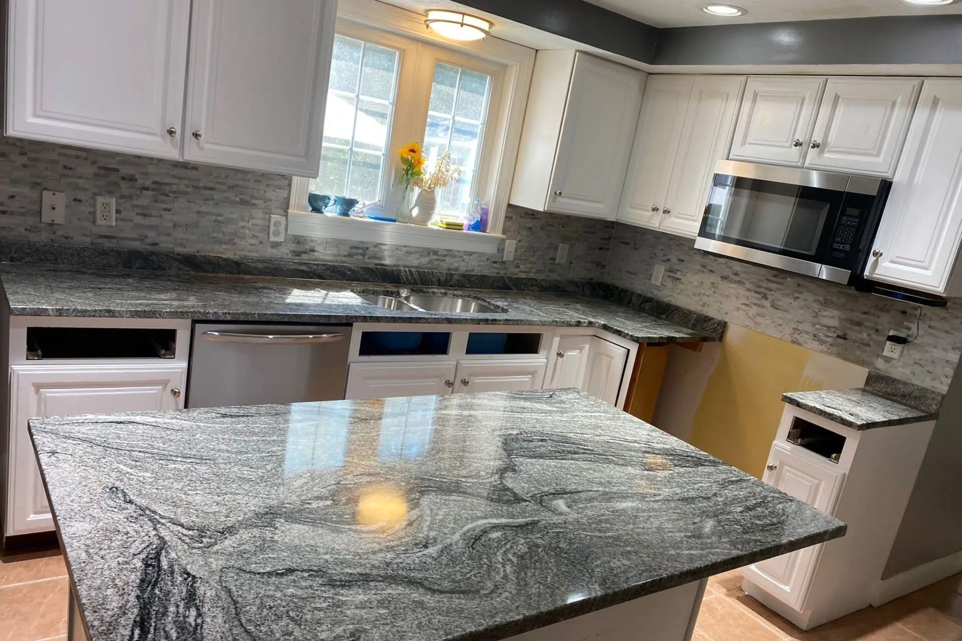 A kitchen with granite counter tops , white cabinets , stainless steel appliances and a large island.
