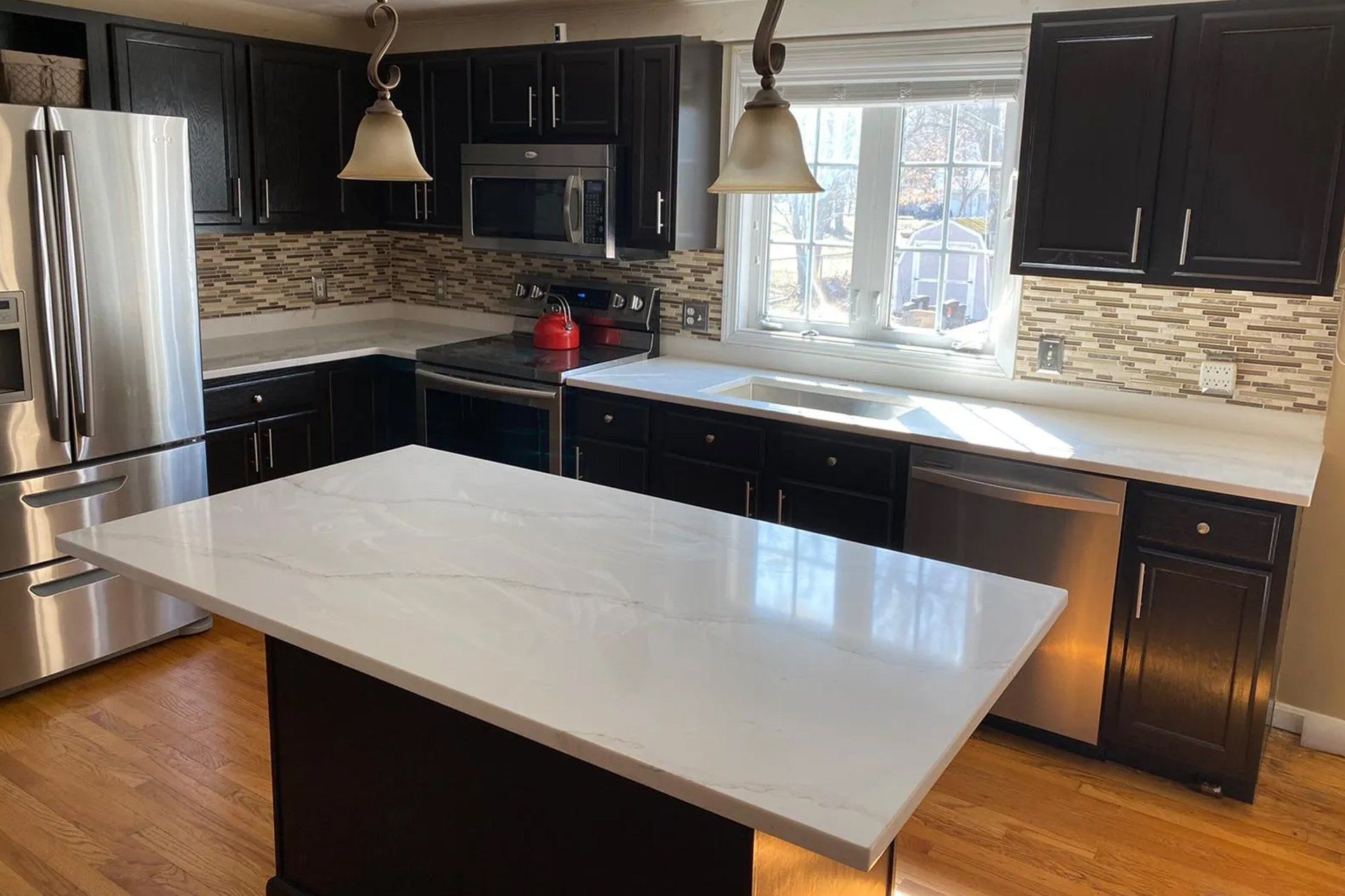 A kitchen with black cabinets and stainless steel appliances and a large island in the middle.