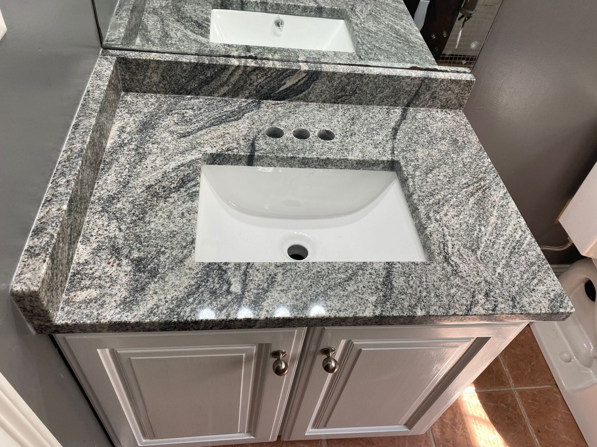 A bathroom sink with a granite counter top and a mirror.