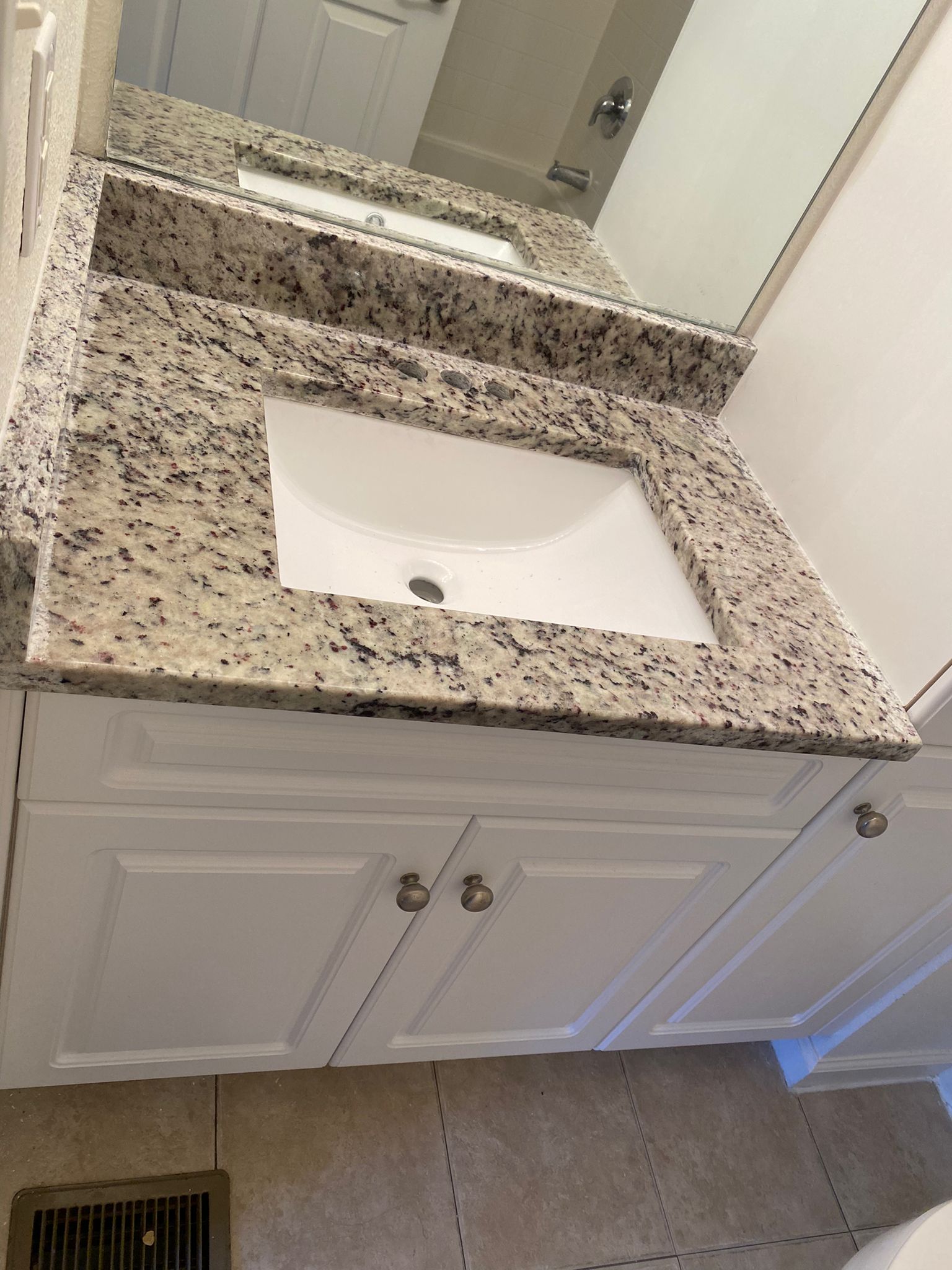 A bathroom sink with a granite counter top and a mirror.