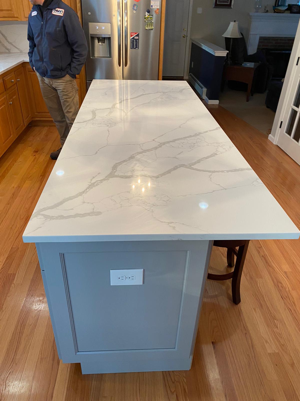 A man is standing next to a large white counter top in a kitchen.