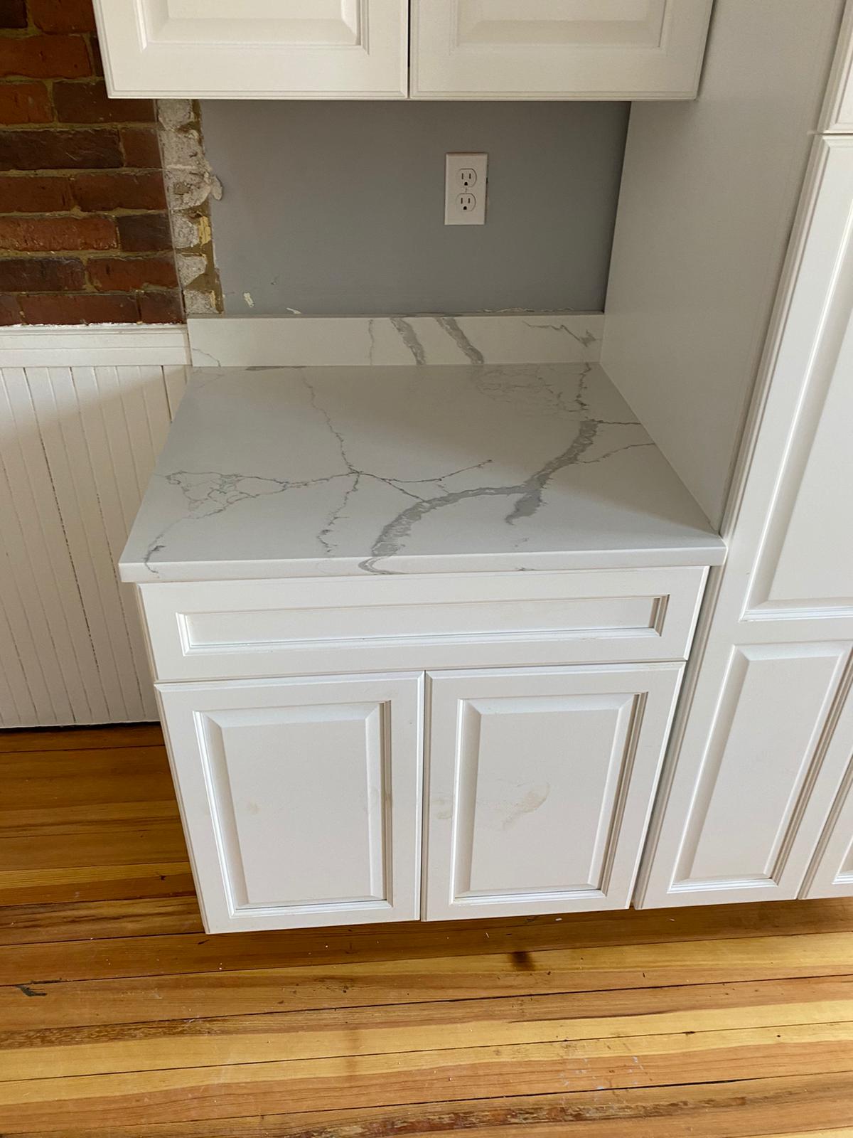 A kitchen with white cabinets and a marble counter top.