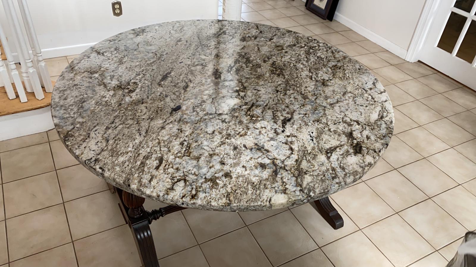 A round granite table is sitting on a tiled floor in a living room.