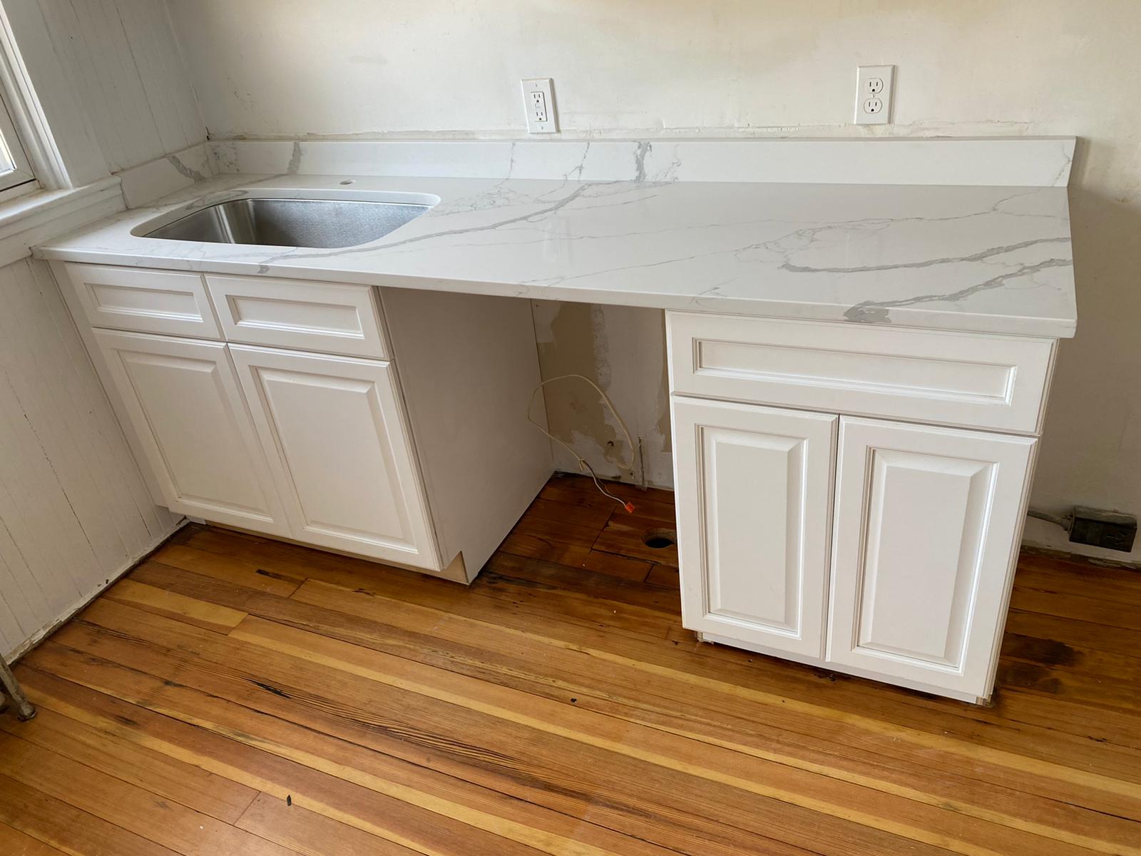 A kitchen with white cabinets , a marble counter top , and a sink.