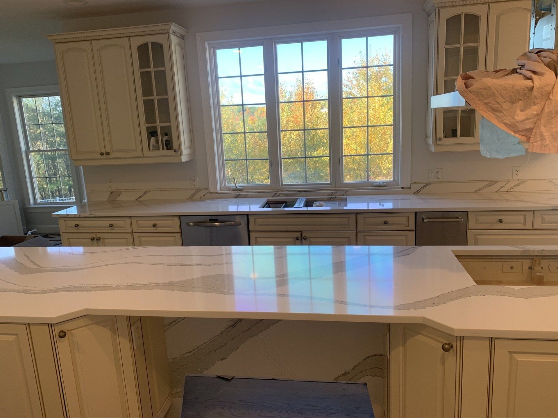 A kitchen with white cabinets , white counter tops , a sink and a window.