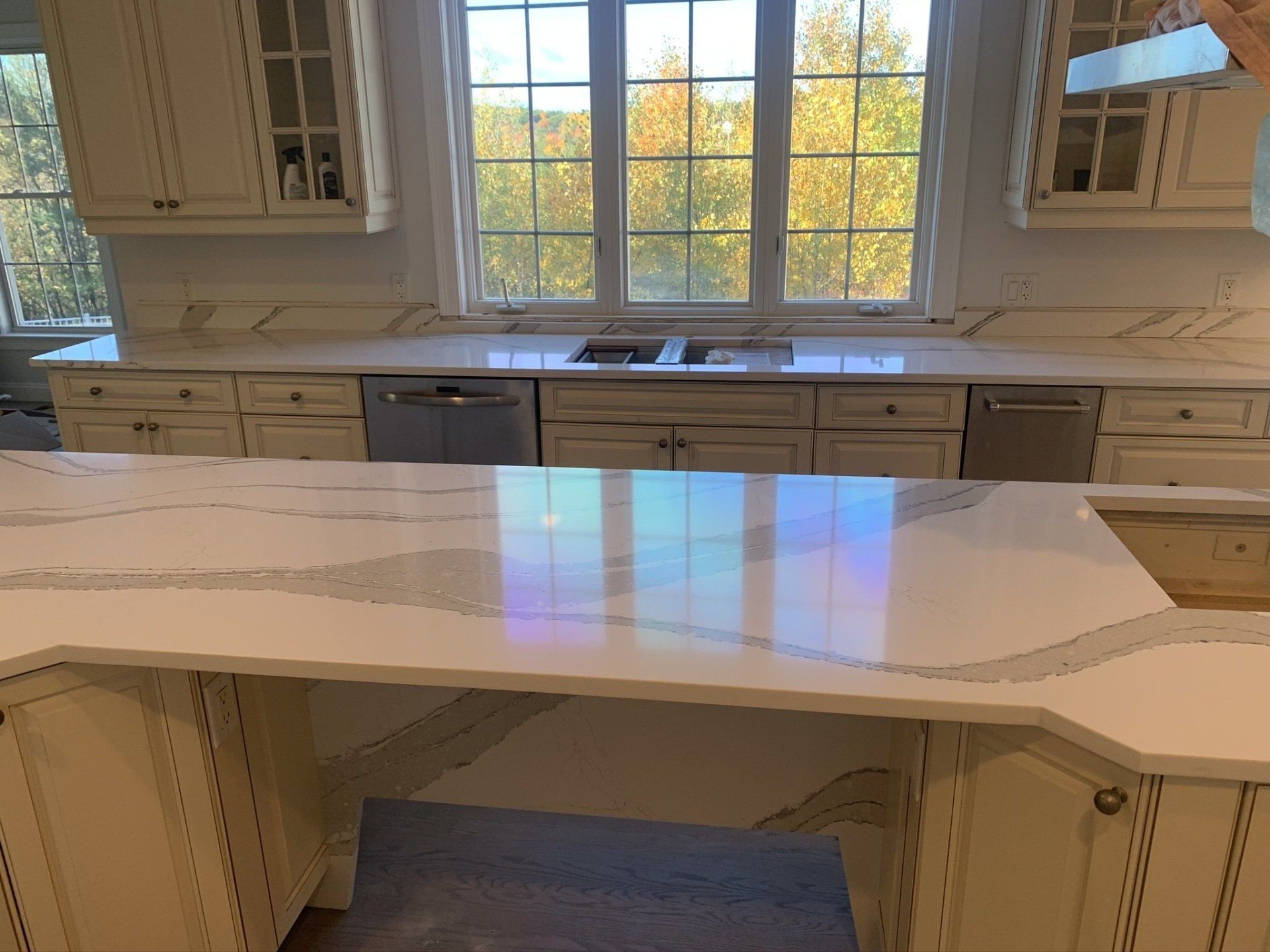 A kitchen with white cabinets , a large island , a sink , and a window.