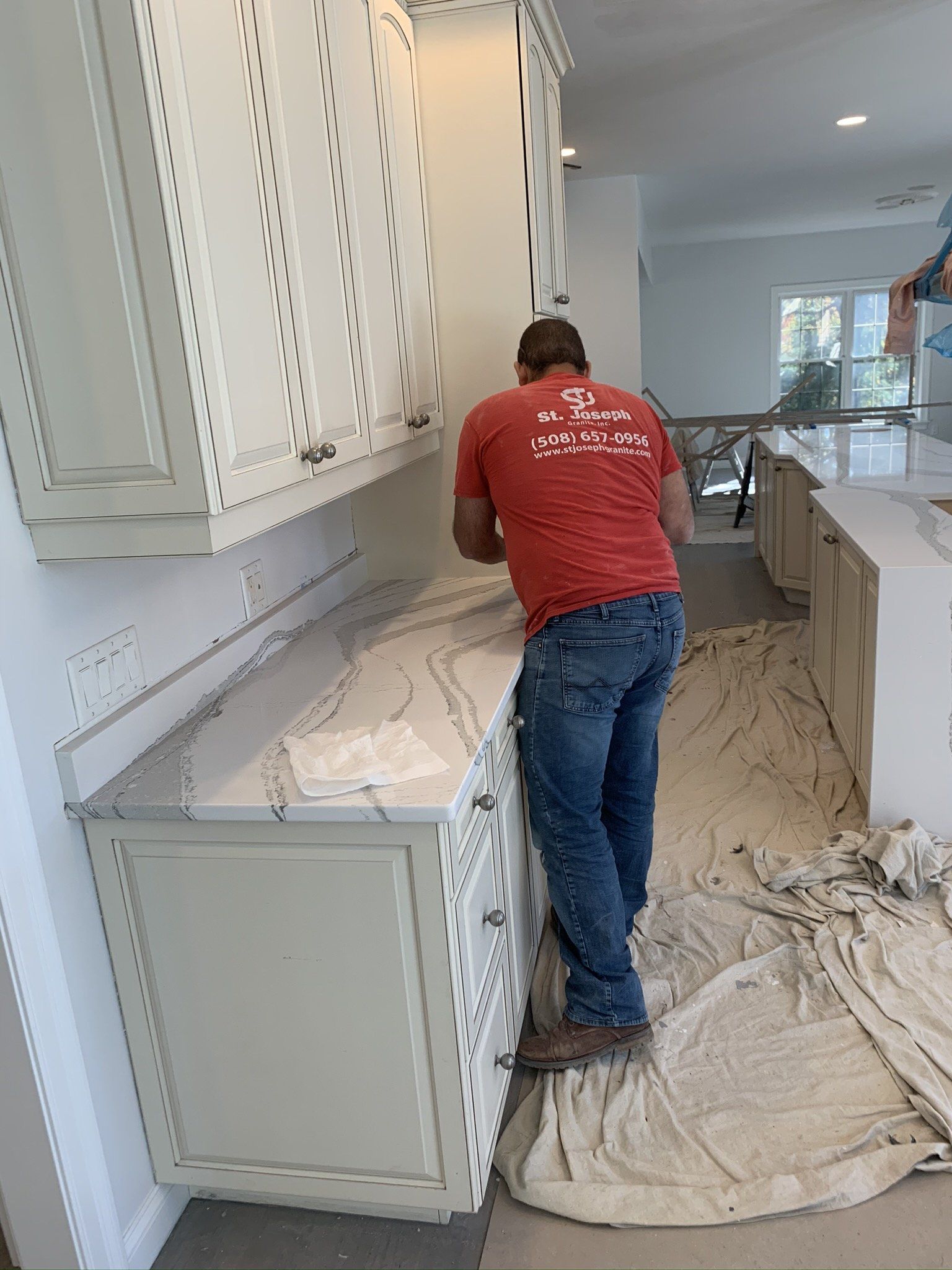 A man in a red shirt is standing next to a counter in a kitchen.