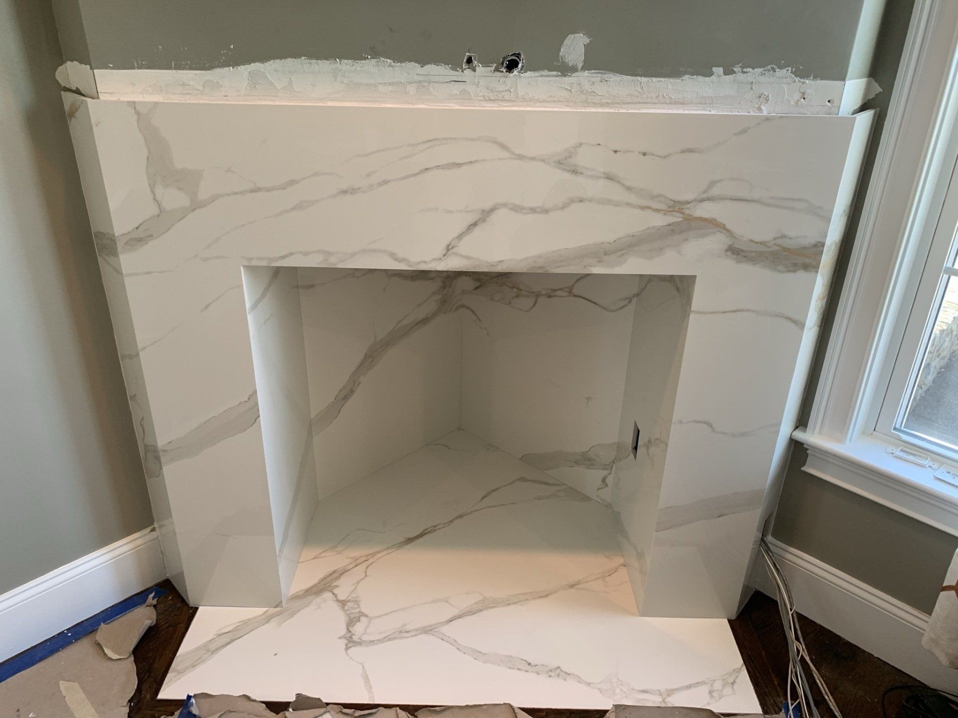 A white marble fireplace is being built in a living room.