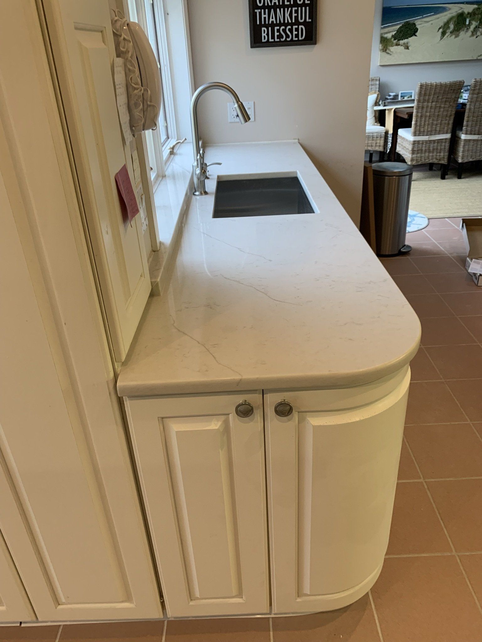 A kitchen with white cabinets , a sink , and a sign on the wall.