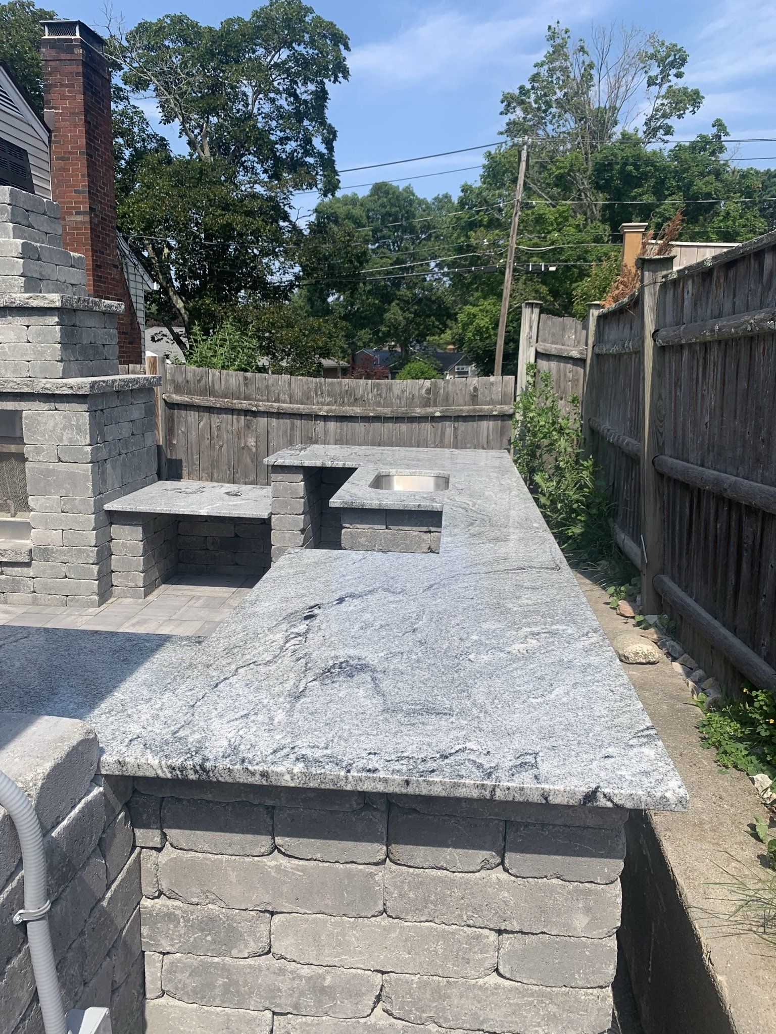 A brick wall with a granite counter top and a wooden fence in the background.