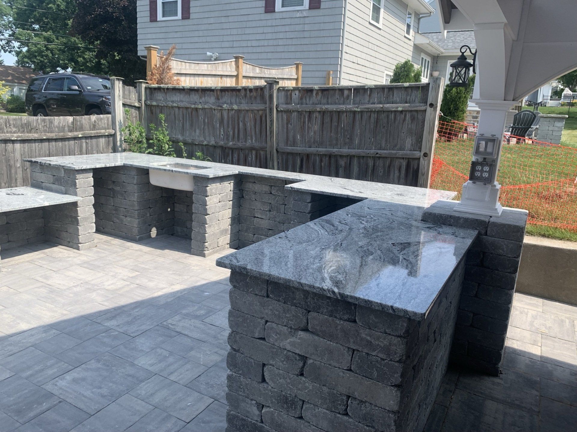 A brick outdoor kitchen with a sink and a fence in the background.