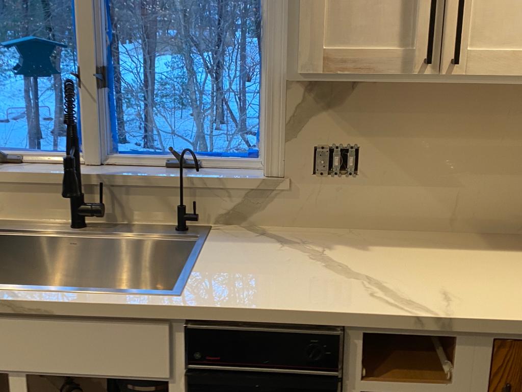 A kitchen with a stainless steel sink and a white counter top.