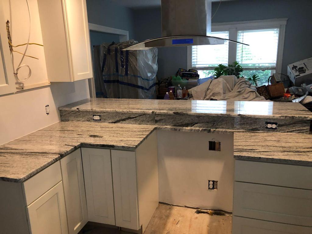 A kitchen with granite counter tops , white cabinets , and a stainless steel hood.