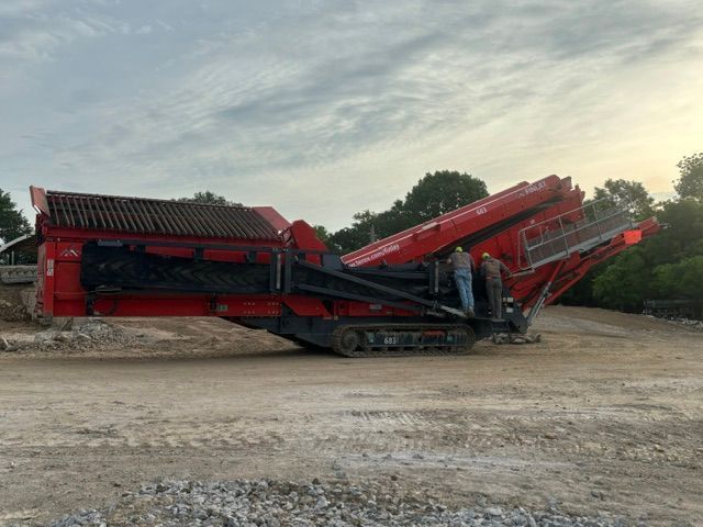Red quarry crusher machine with conveyor arms on a gravel lot at dusk