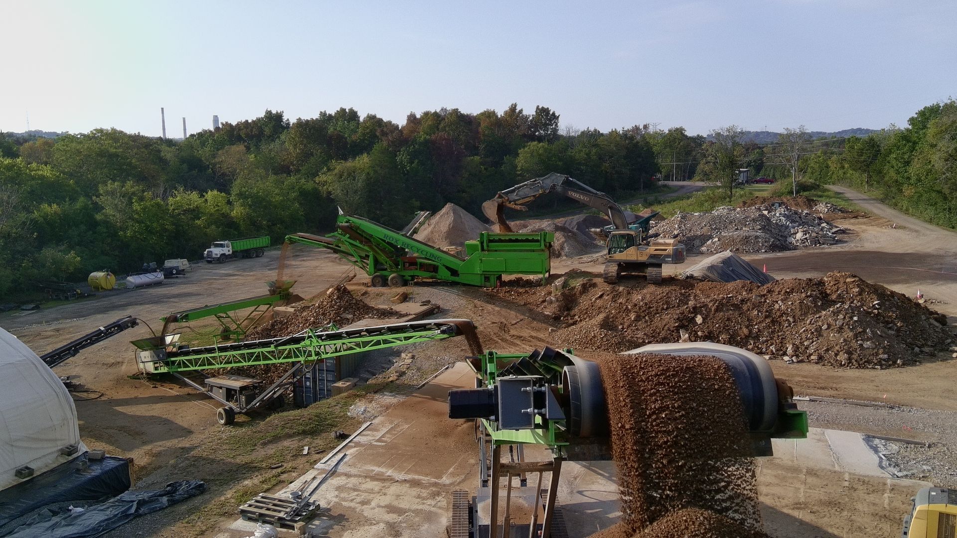Construction site with excavators, piles of dirt, and a conveyor belt under a clear sky