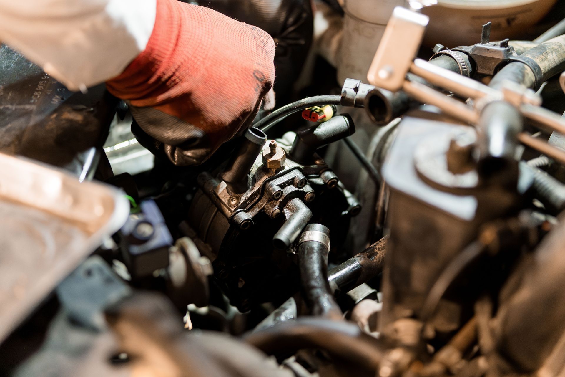 A person in red gloves works on a car engine, hands visible, engine bay in the background.