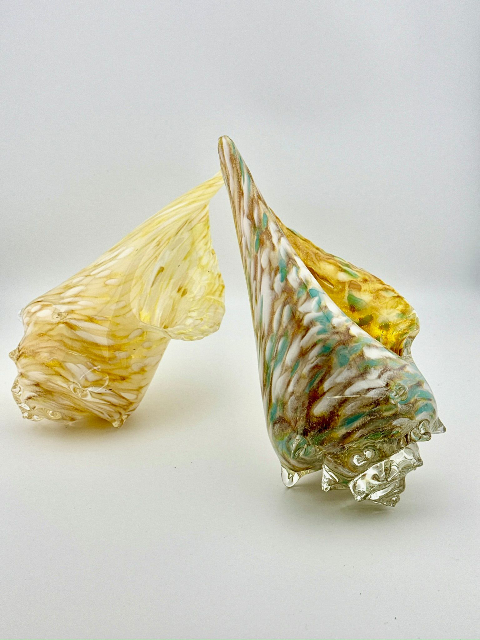 Two decorative glass cone-shaped sculptures, one pale yellow and one clear with green and gold accents.