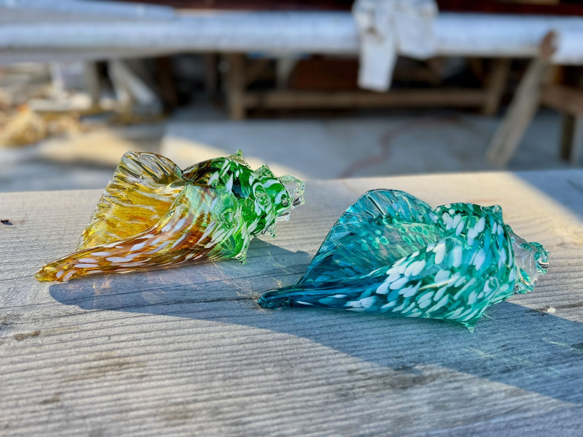 Two colorful glass sculptures, one amber-green and one teal, on a weathered wooden surface.
