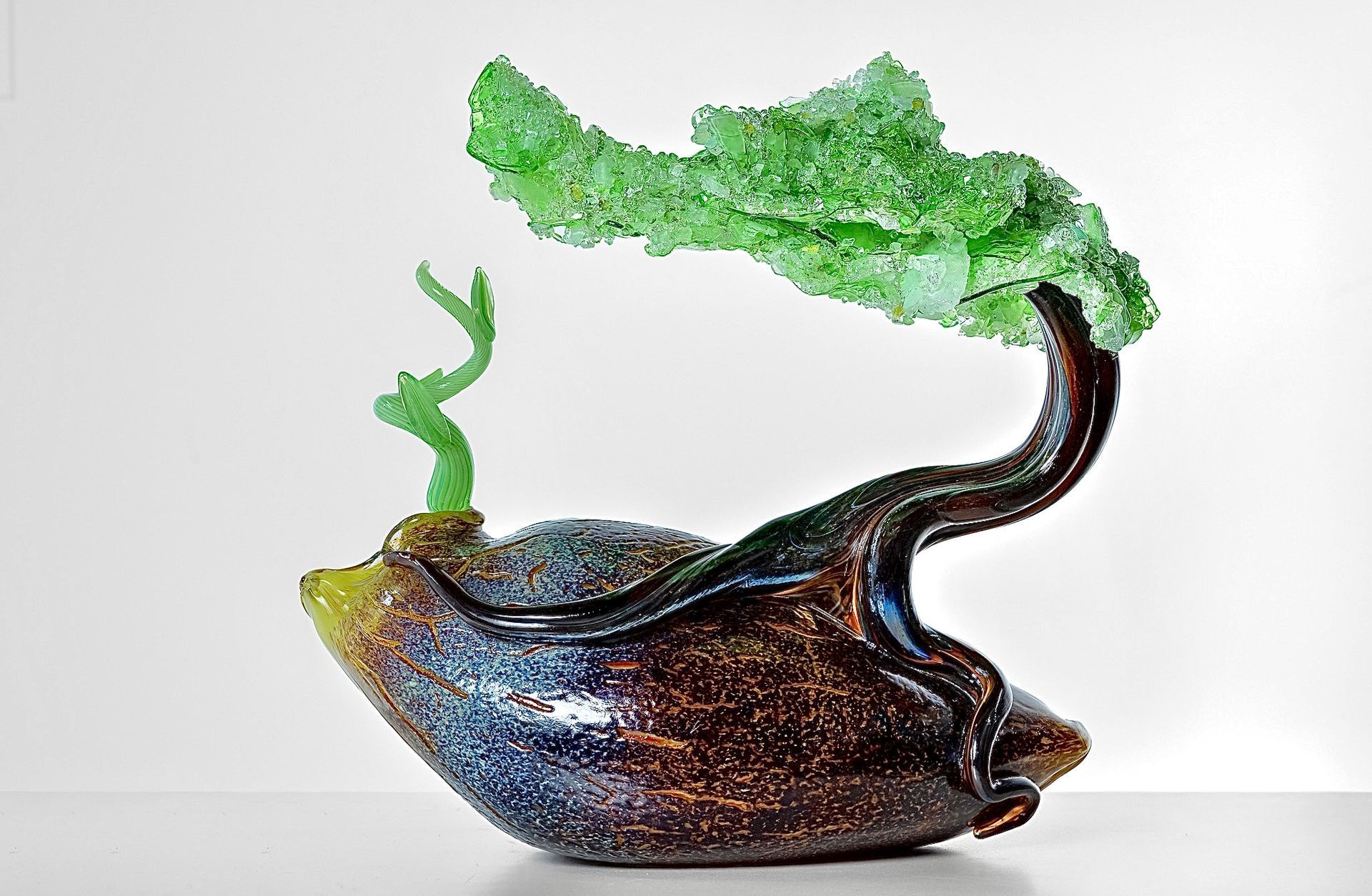 Abstract glass sculpture with green leaf-like top and dark glossy base on a white background