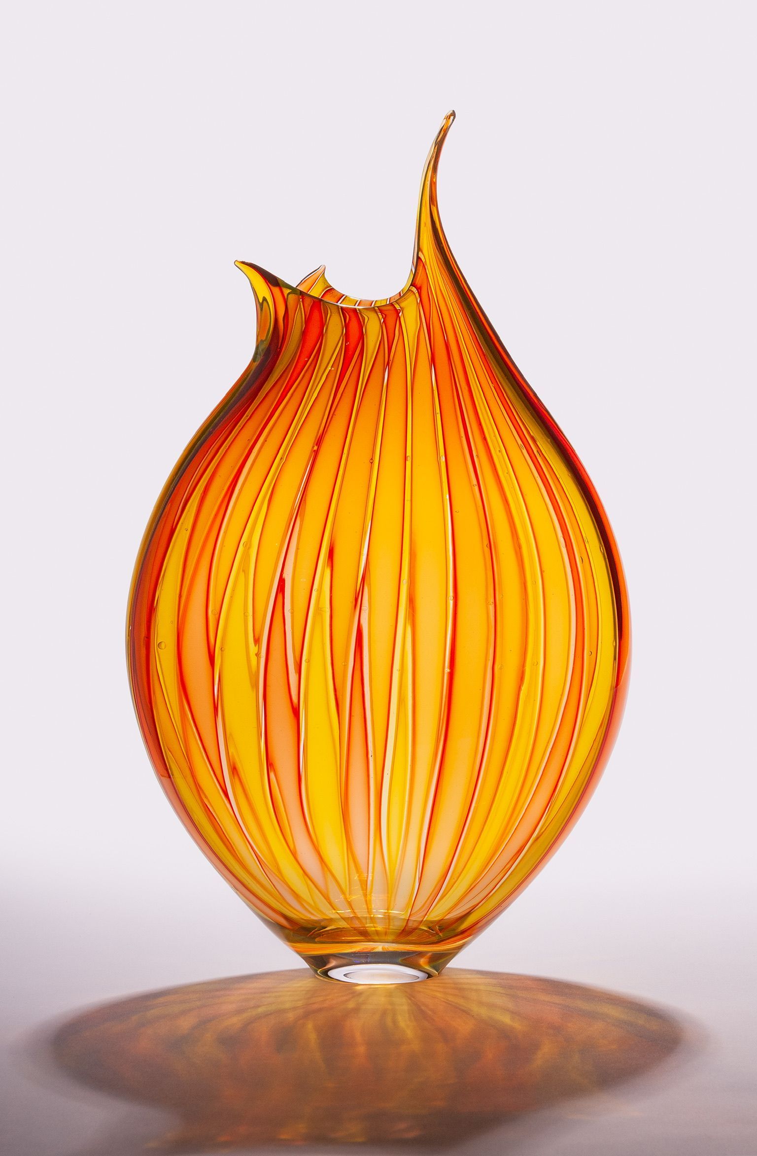Orange glass vase with swirling amber stripes and a flared top, on a reflective surface