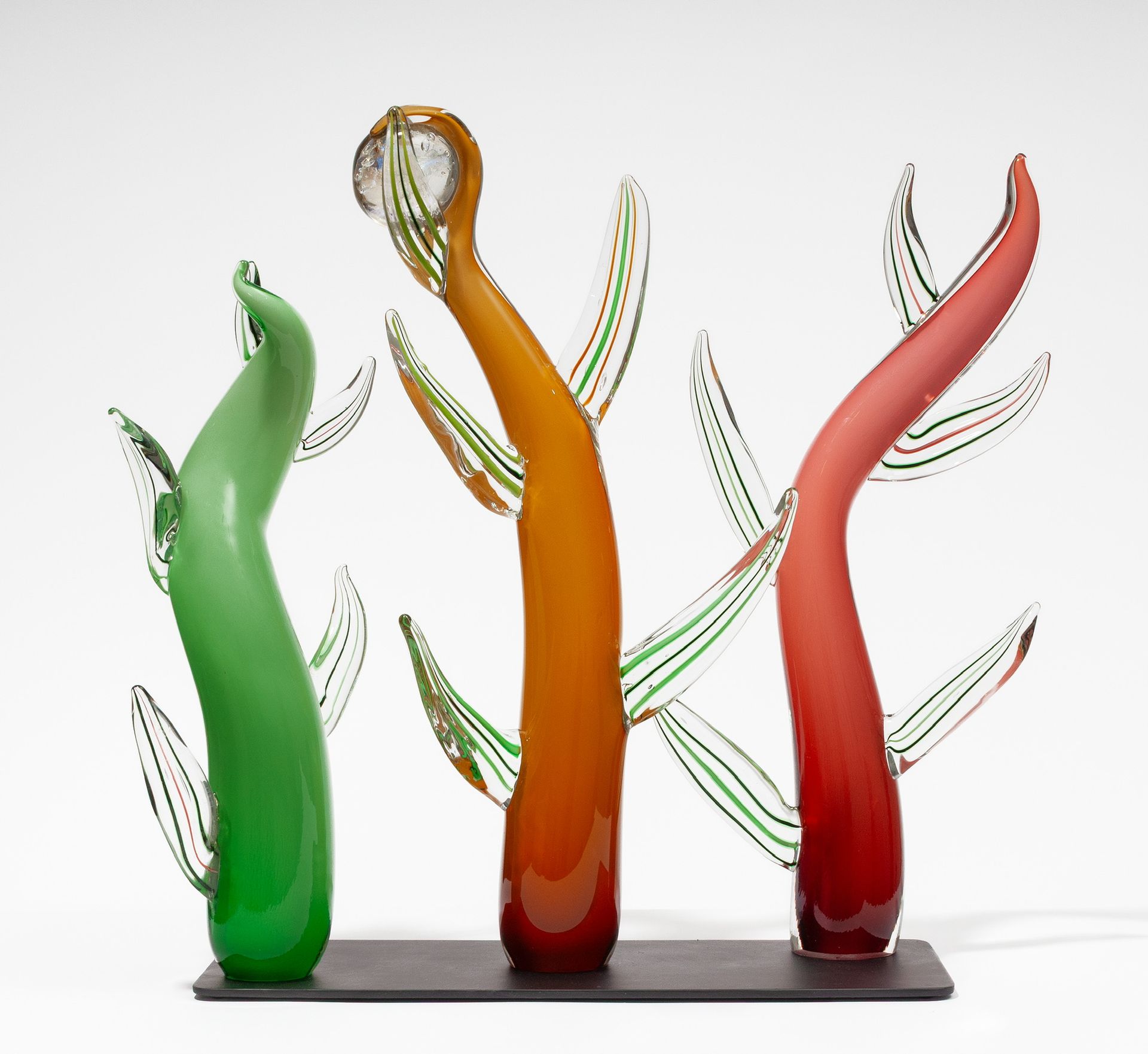 Three abstract glass-like sculptures in green, orange, and red on a white background