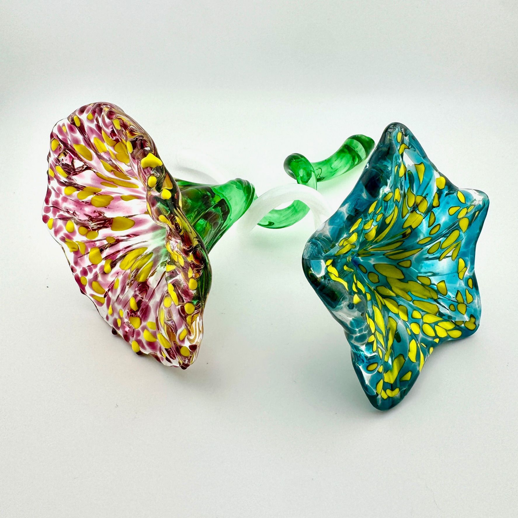 Two colorful abstract glass ornaments, pink-yellow on the left and blue-yellow on the right, on a white background