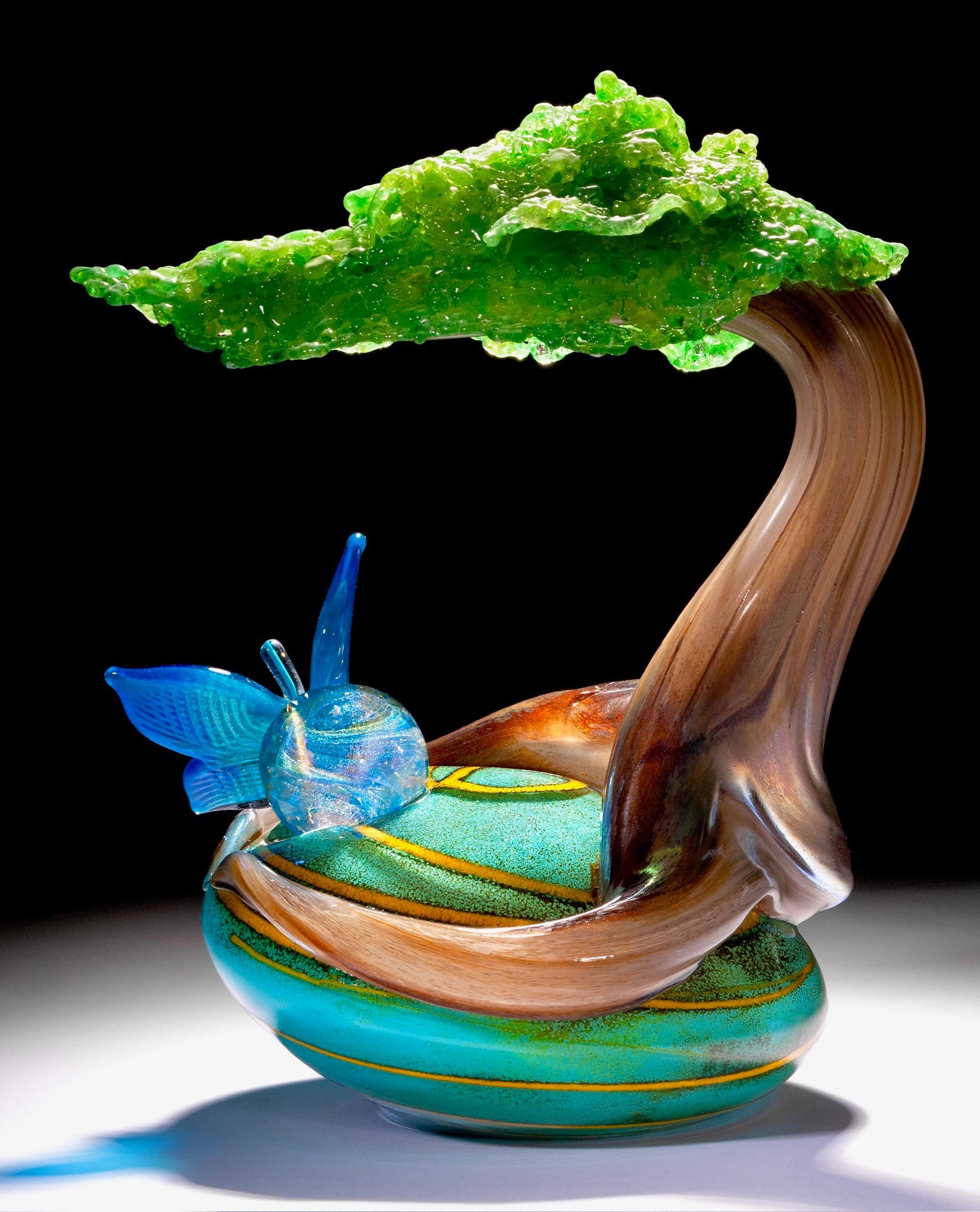 Colorful abstract sculpture with a green tree, brown curved trunk, and a blue butterfly on a striped base