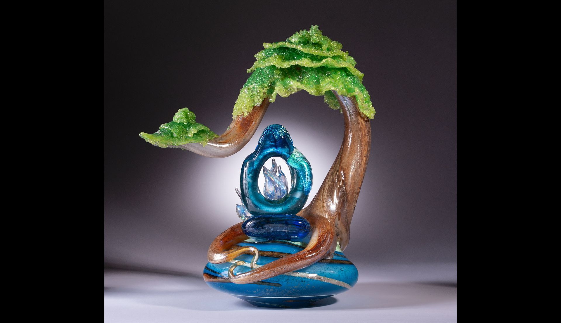 Blue glass sculpture of a tree with a bird perched on a branch, on a gray background