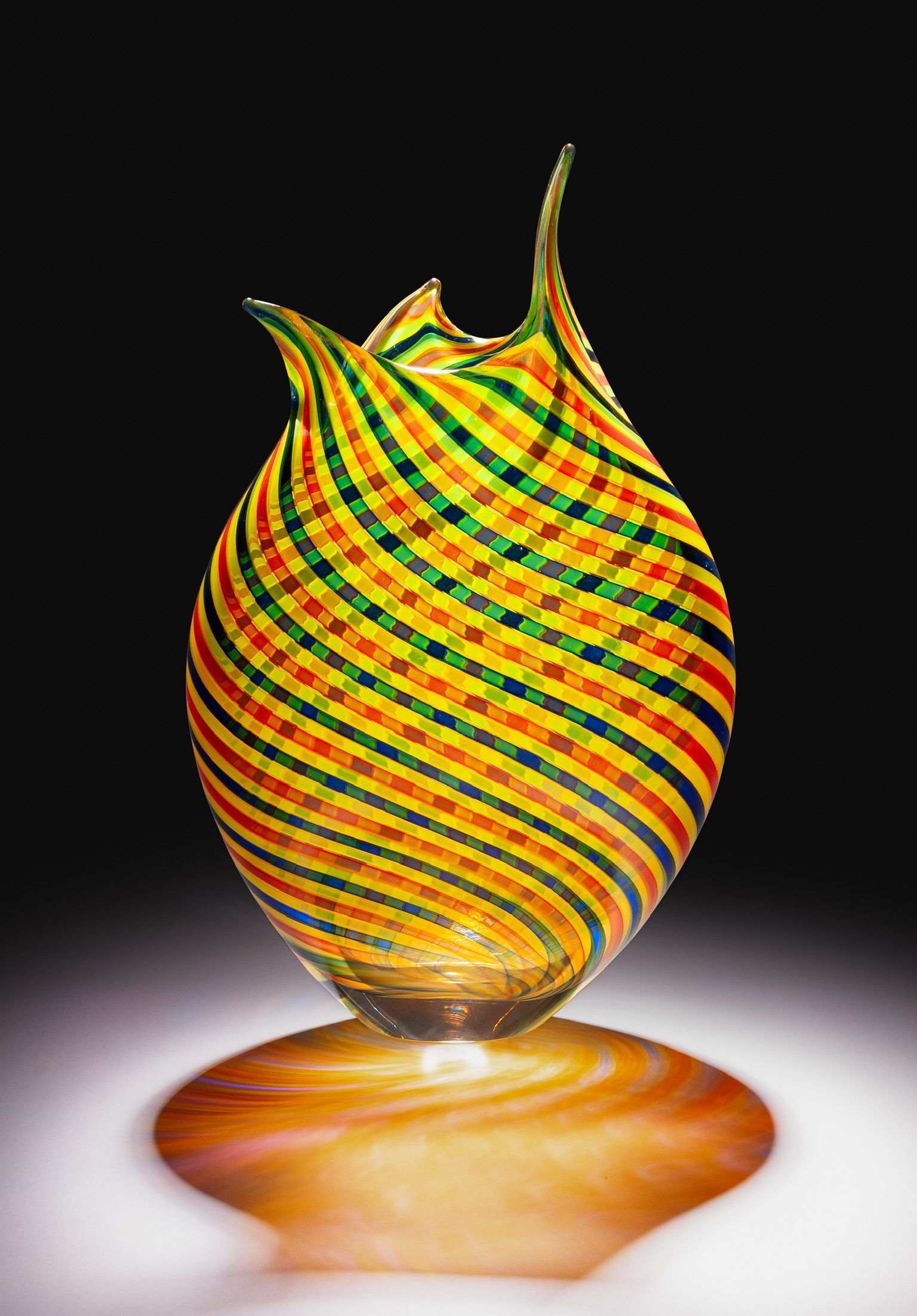 Striped multicolor glass vase with flared spiky rim on a warm-toned base against a black background