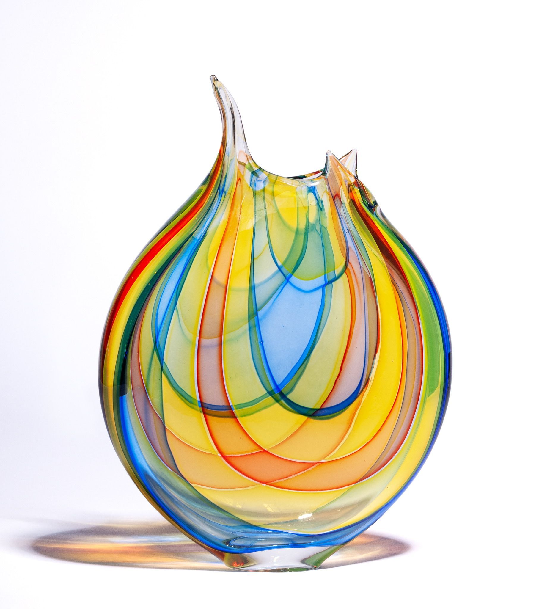 Multicolored glass sculpture with teardrop shape and amber shadow on a white background