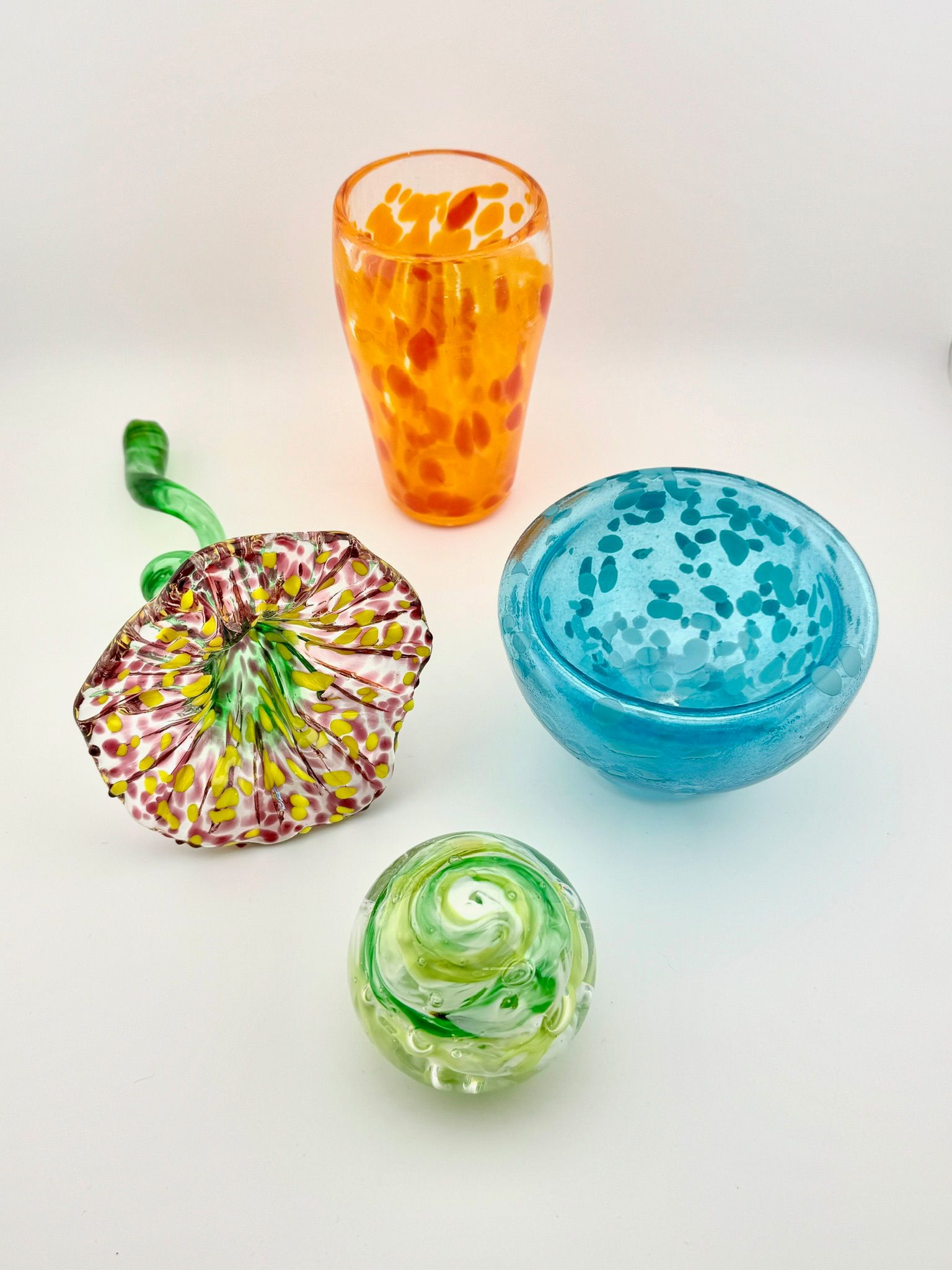 Four colorful glass bowls and dishes on a white background, including orange, blue, green, and multicolored pieces