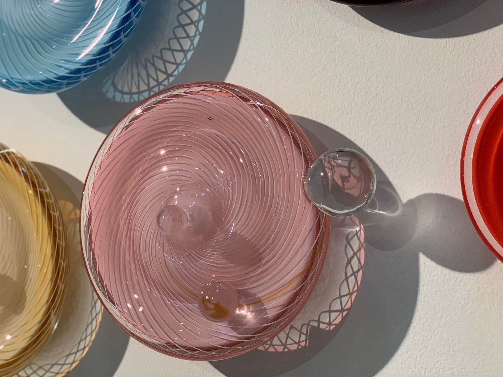 Assorted colorful glass bowls and cups on a light surface, including pink, blue, yellow, and red pieces.