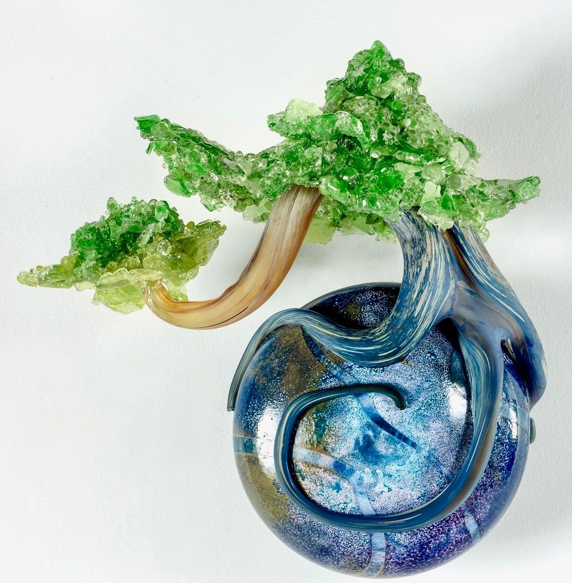 Blue glass sculpture of a tree with green leaves on a white background
