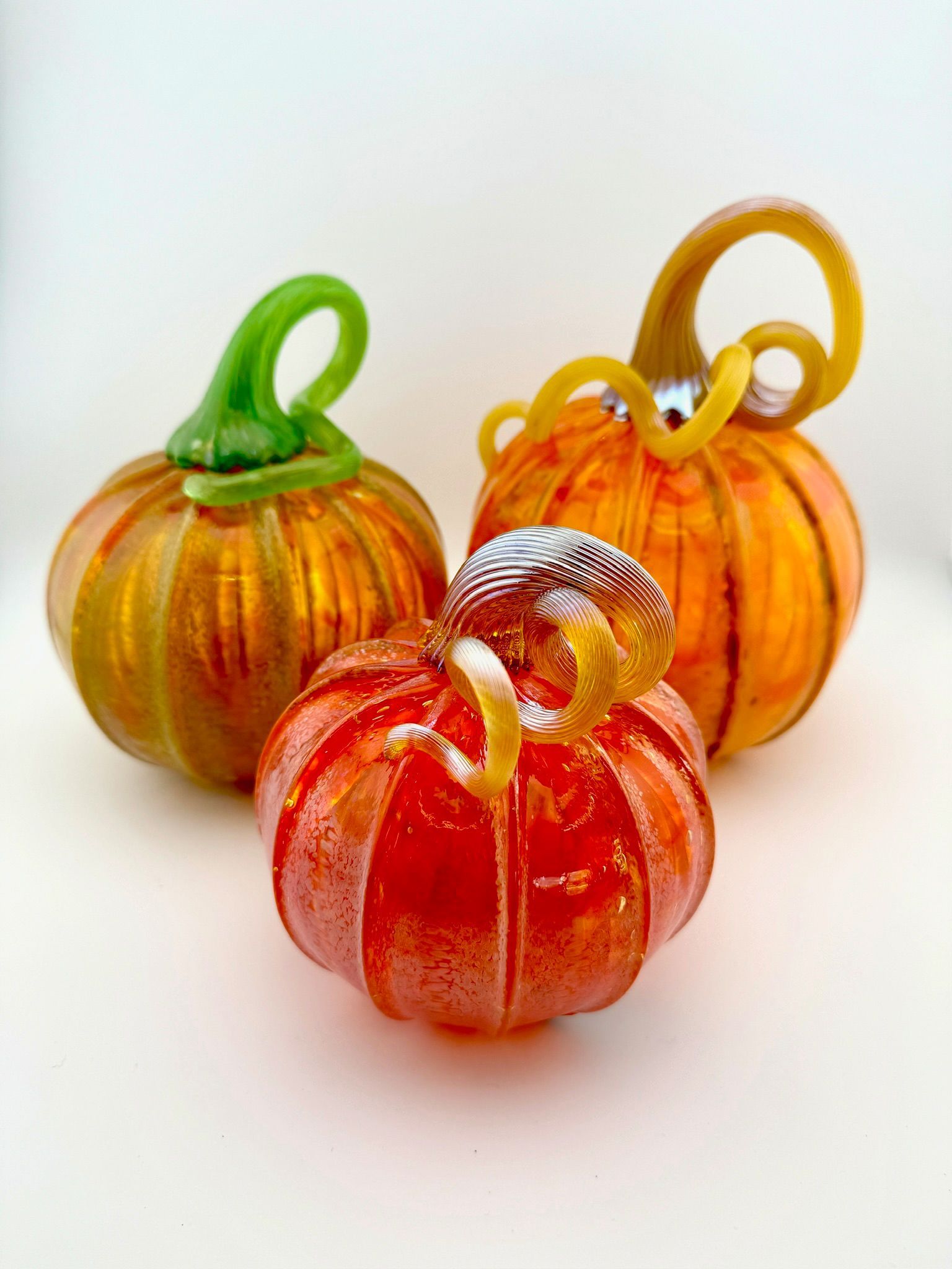 Three small glass pumpkin ornaments in green, orange, and red on a white background