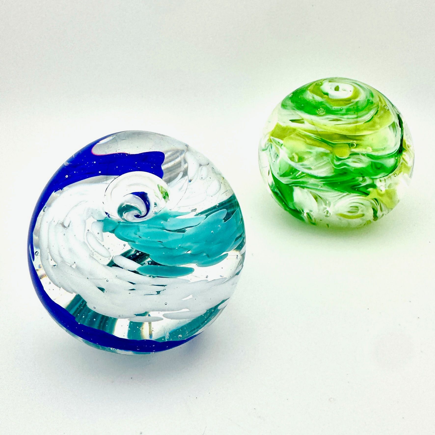 Two glass marbles, one blue-white and one green-white, on a white background
