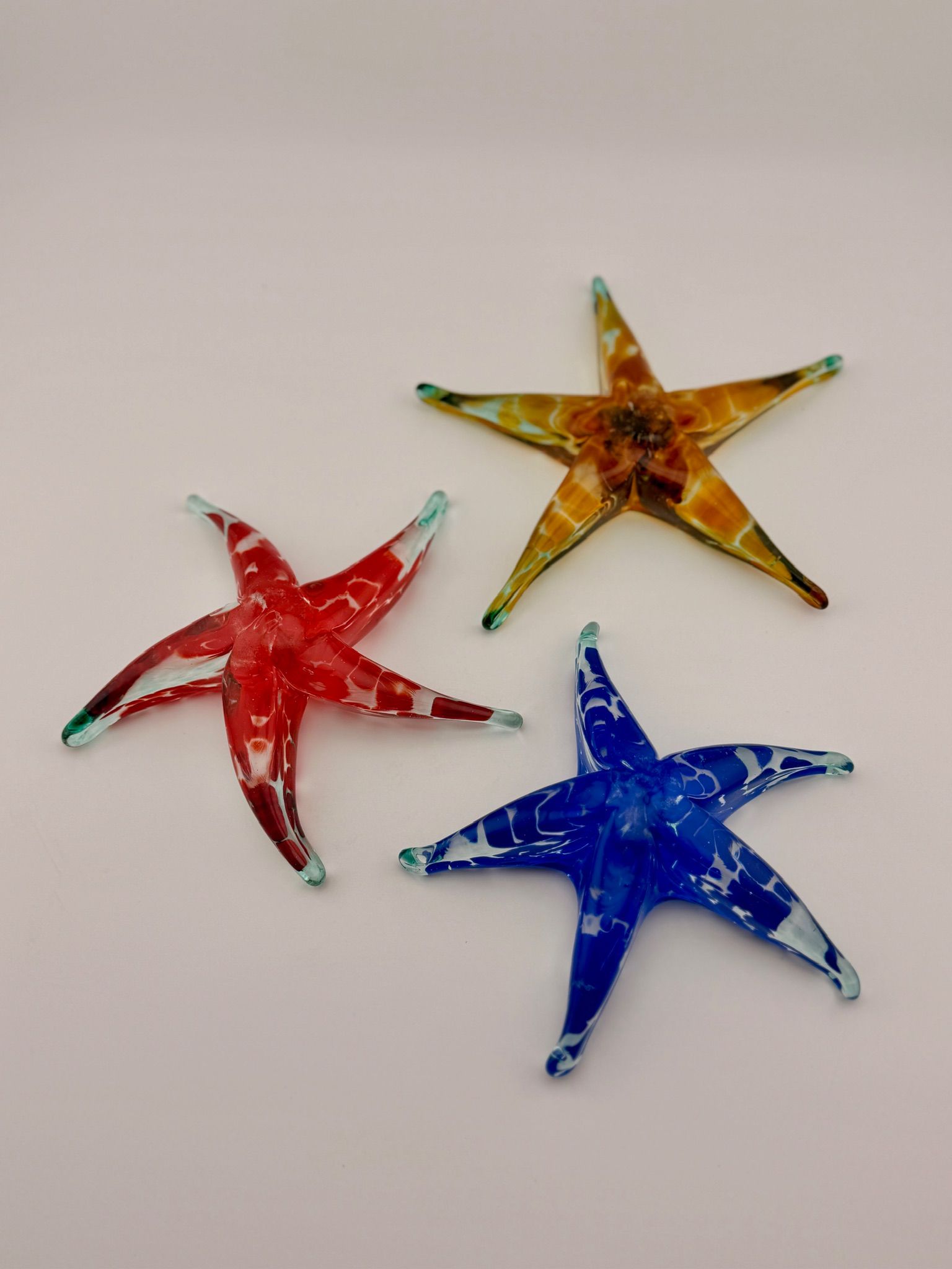 Three colorful starfish-shaped ornaments in red, gold, and blue on a white background