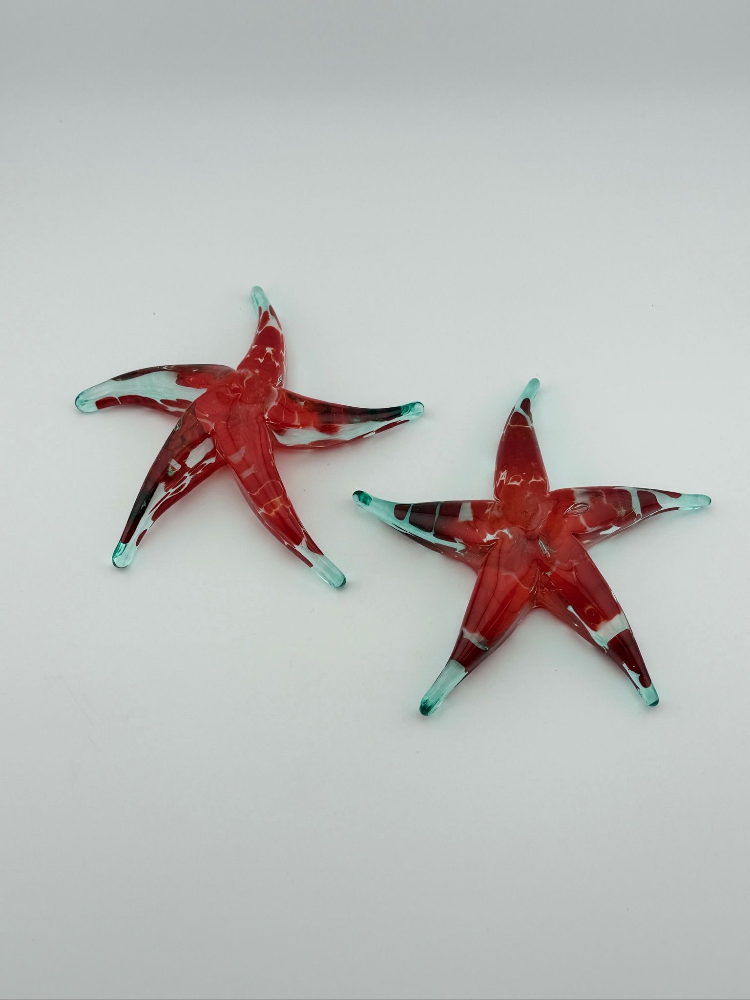 Two red and turquoise starfish on a light gray background