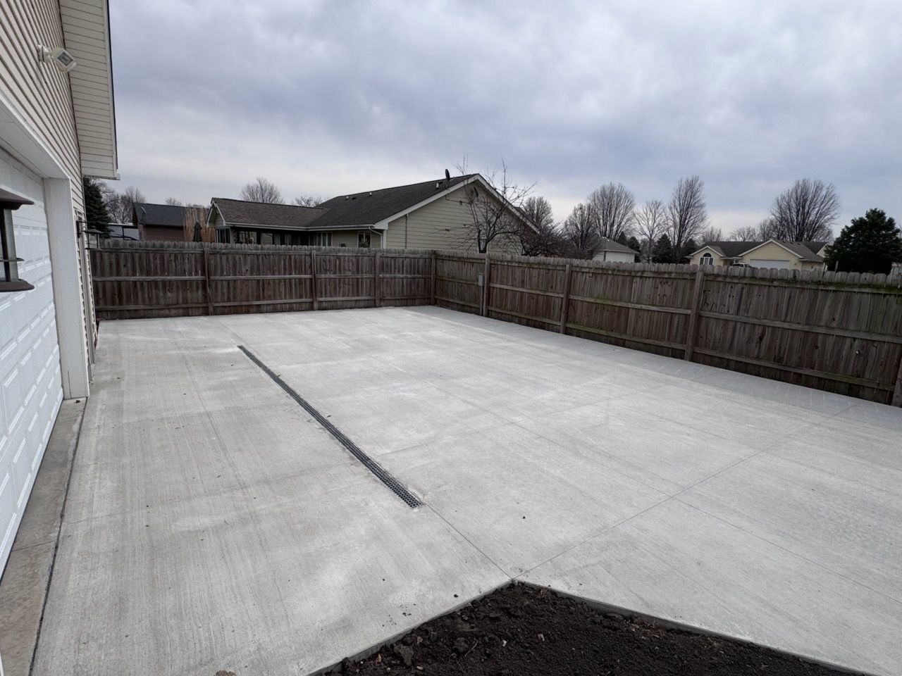 Empty concrete backyard patio with wooden fence and overcast sky