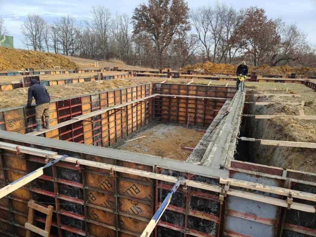Construction site with concrete foundation formwork and workers on muddy ground