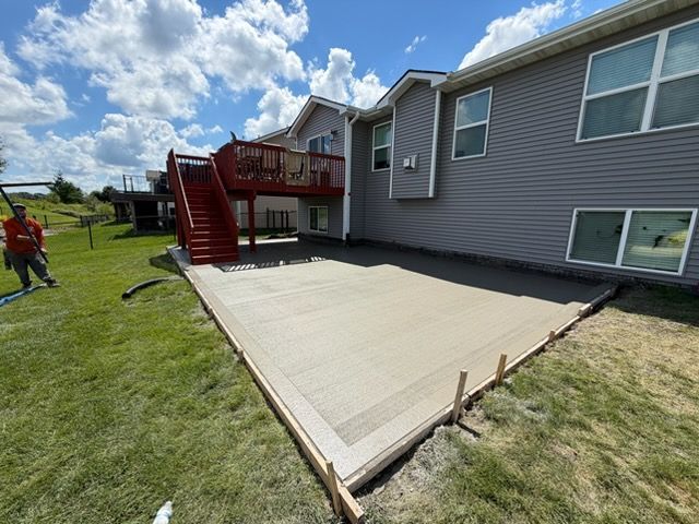 Back patio deck ramp beside gray house, with red stairs and a grassy yard under a cloudy sky