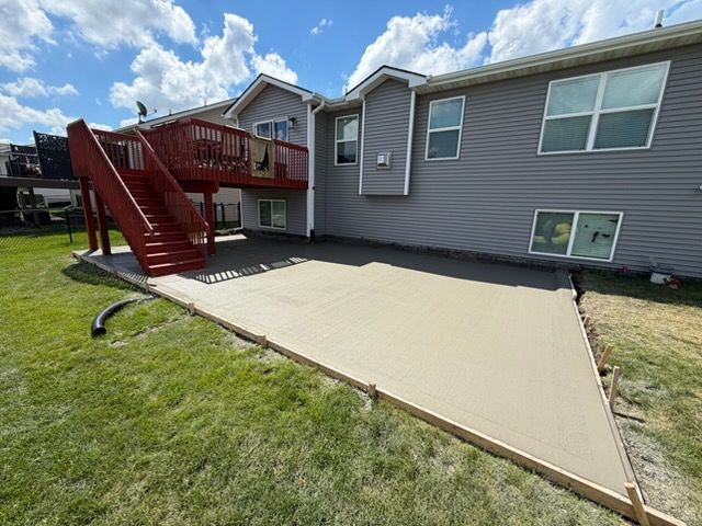 Gray house with red deck stairs and a tan concrete patio in the backyard