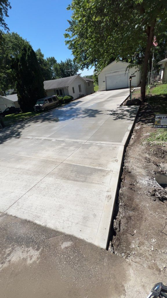 Steep concrete driveway leading to a white garage, with trees and a house on a sunny day