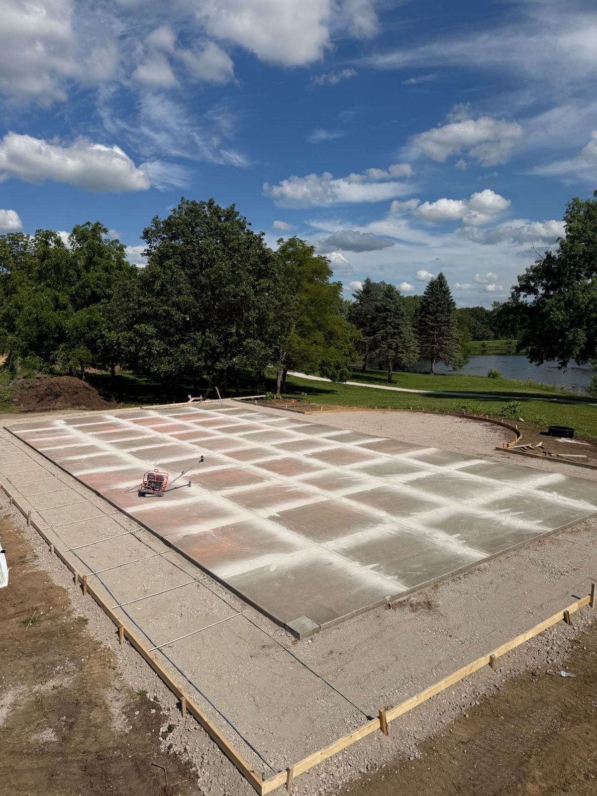 Concrete foundation slab with a white grid layout in a grassy outdoor area under a partly cloudy sky