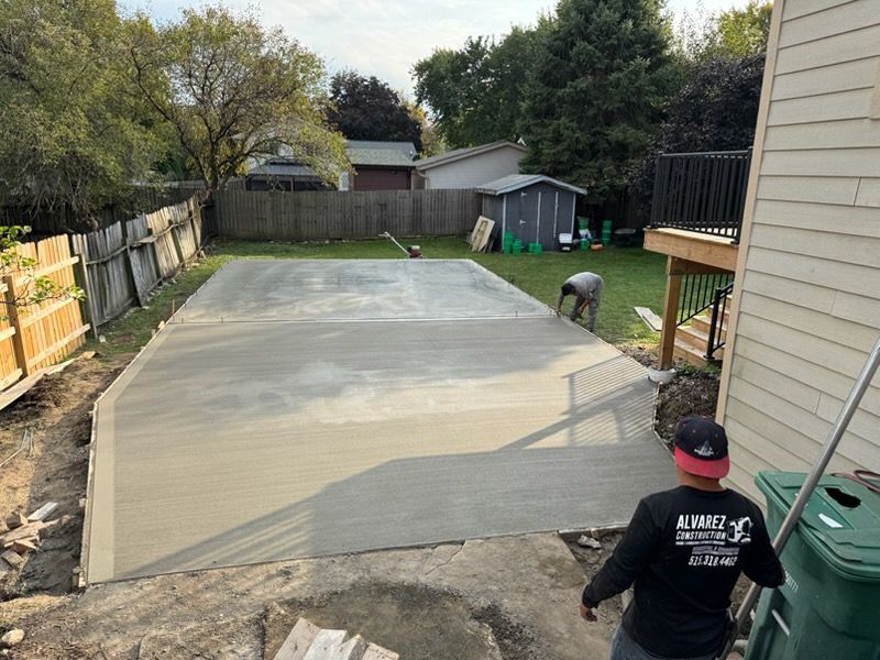 Backyard with a freshly poured concrete slab; one person kneels near the house.