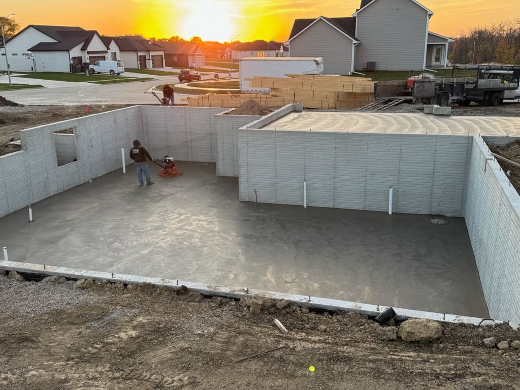 Concrete foundation walls at a construction site at sunset, with workers in the pit and houses nearby