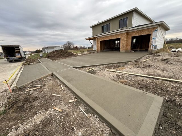 New concrete sidewalk leading to a partially built house on a muddy construction site under cloudy skies