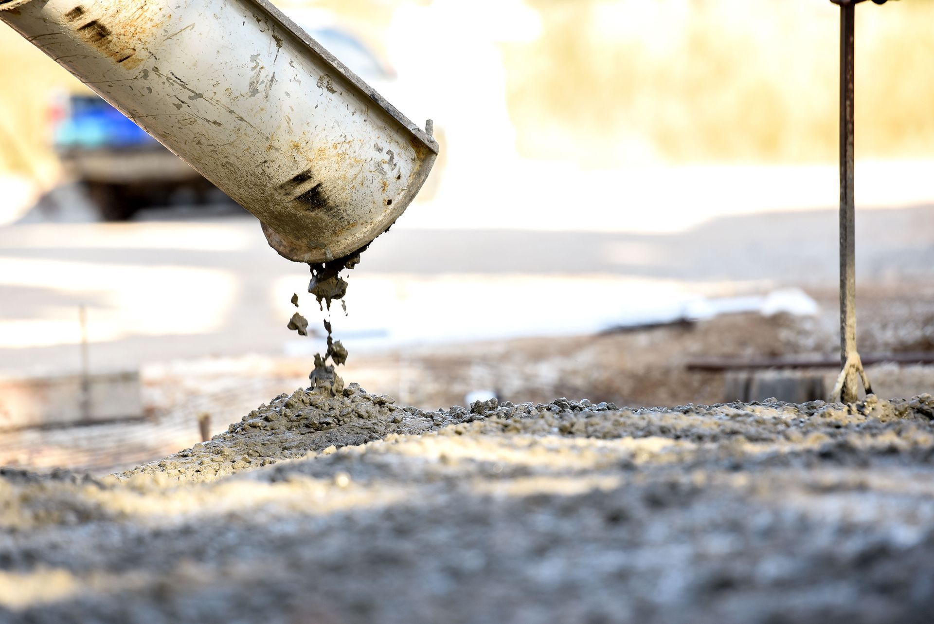 Concrete being poured from a chute onto a gray surface in a construction setting.