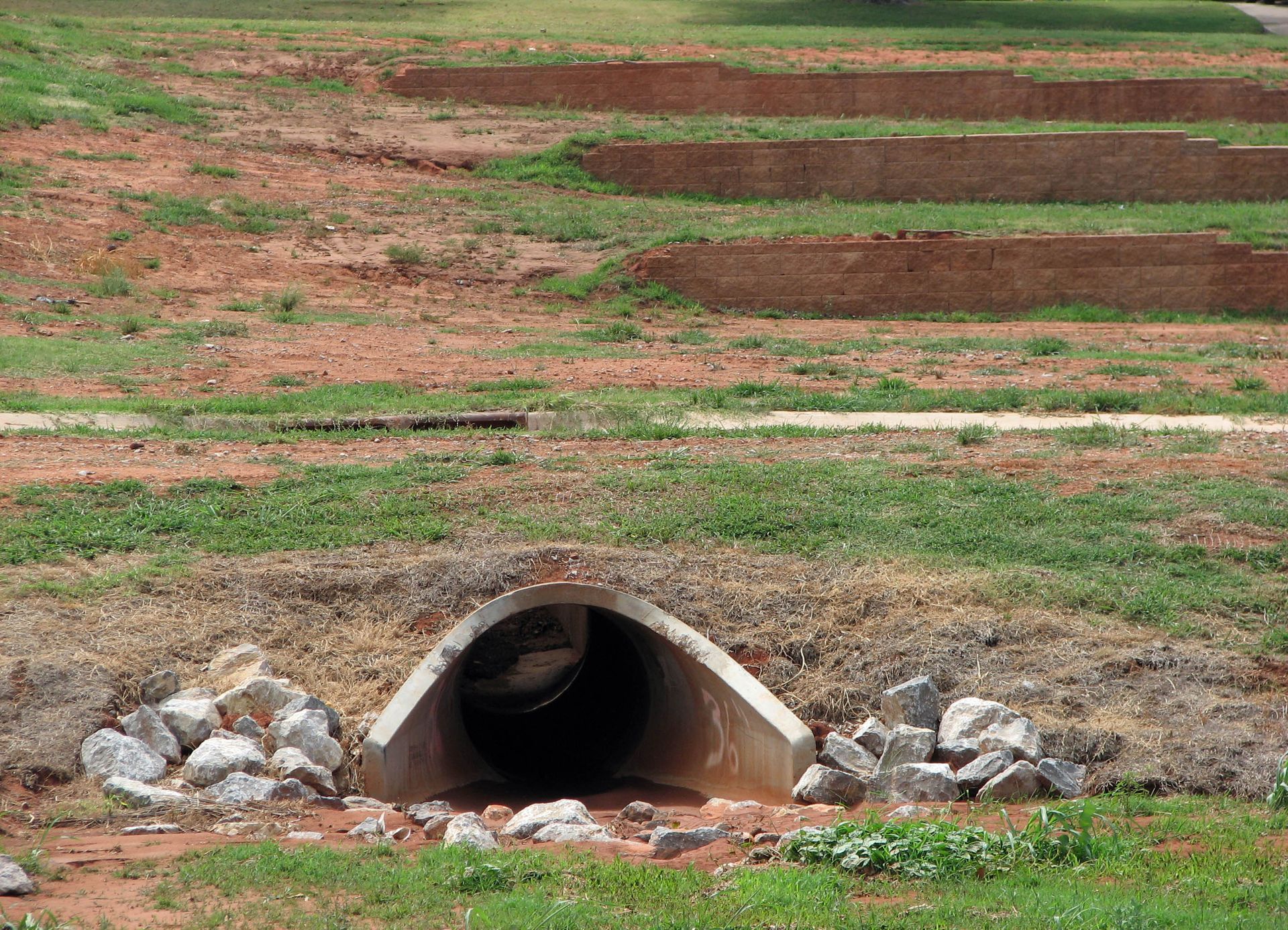 Tunnel entrance under a grassy area with terraced red dirt and small rocks.