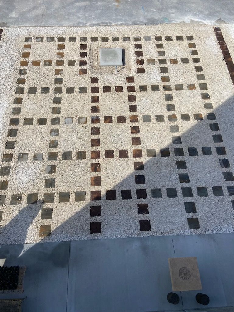 Gridded concrete floor with darker square accents, near a rectangular access panel and small table.